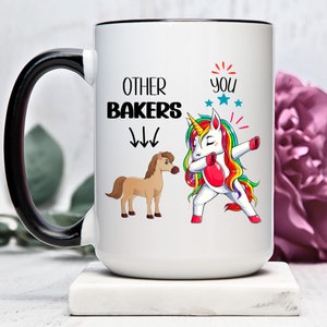 Puede incluir: Taza de cerámica blanca con asa negra. La taza presenta un unicornio colorido haciendo un dab con el texto "OTHER BAKERS" y flechas apuntando hacia abajo a un caballo marrón. El texto "YOU" con estrellas está por encima del unicornio.