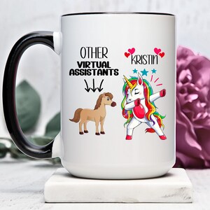 May include: White ceramic mug with a black handle. The mug has a black rim and features a unicorn doing the dab with the text "OTHER VIRTUAL ASSISTANTS" and arrows pointing down to a brown horse. The text "KRISTIN" is written above the unicorn with two pink hearts on either side.