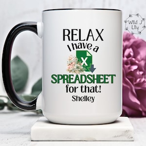 May include: White ceramic mug with a black handle and rim. The mug has a green and white spreadsheet icon with the text "Relax I have a spreadsheet for that! Shelley".