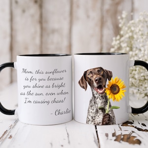 May include: White ceramic coffee mug with a black rim and handle. The mug features a brown and white dog holding a yellow sunflower. The text on the mug reads "Mom, this sunflower is for you because you shine as bright as the sun, even when I'm causing chaos! - Charlie."