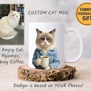 May include: A white ceramic mug featuring a cat wearing blue pajamas and holding a coffee cup. The mug is on a wooden coaster. Text on the mug says "CUSTOM CAT MUG" and "FUNNY & PERSONALIZED GIFT". Additional text reads "Your Angry Cat. In Pajamas. Drinking Coffee."