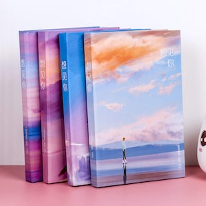 May include: A set of five notebooks with a sky and water background. The notebooks have a light blue, purple, and pink color scheme. The text on the front of the notebooks says "I wanna see you" and "想见你" which translates to "I want to see you".