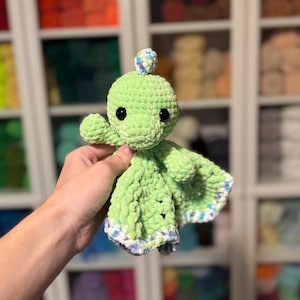 Puede incluir: Un pulpo de crochet verde con una cabeza con estampado azul y blanco. El pulpo tiene una textura suave y mullida y es un gran juguete para beb&eacute;s y ni&ntilde;os peque&ntilde;os.