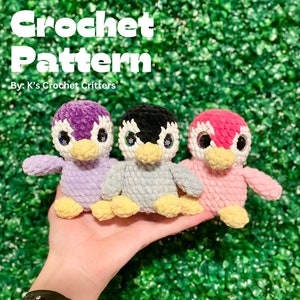 May include: Three crocheted penguin amigurumi toys in purple, gray, and pink. Each penguin has a yellow beak and large, white googly eyes. The penguins are sitting on a hand.