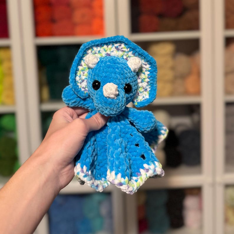 Puede incluir: Un dinosaurio de peluche de crochet azul con detalles blancos y verdes. El juguete tiene una textura suave y afelpada y es perfecto para acurrucarse.