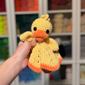 Puede incluir: Un juguete de peluche de pato amarillo tejido a crochet con detalles naranjas. El juguete tiene una textura suave y esponjosa y es perfecto para acurrucarse.