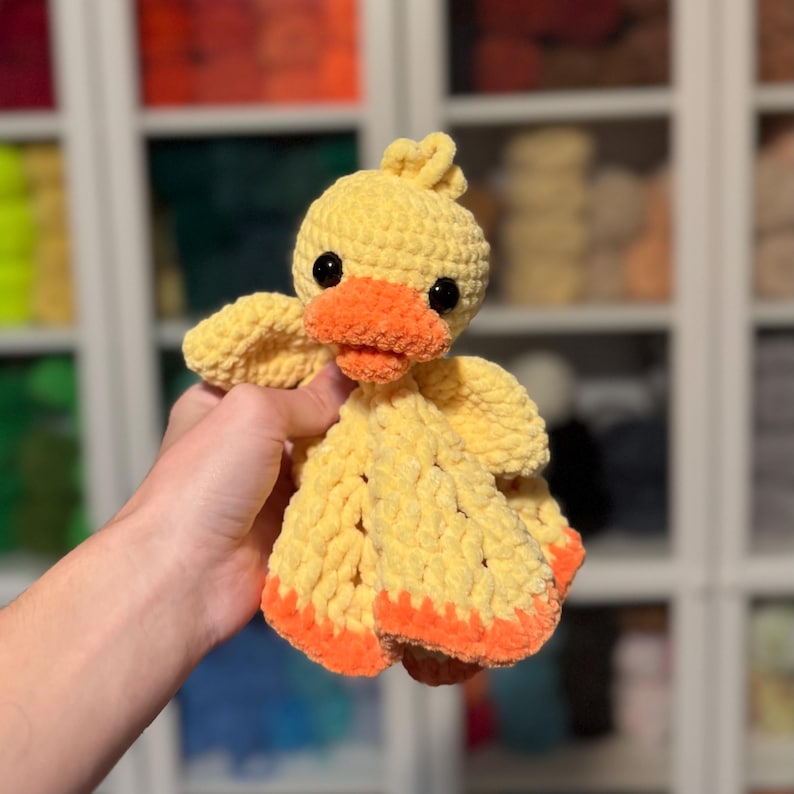 Puede incluir: Un juguete de peluche de pato amarillo tejido a crochet con detalles naranjas. El juguete tiene una textura suave y esponjosa y es perfecto para acurrucarse.