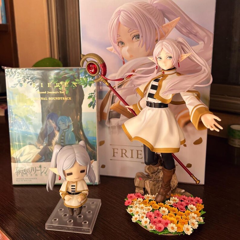 May include: A collection of anime-themed figurines and a soundtrack album. The main figurine is a character with long white hair, wearing a white and gold outfit, and holding a staff. A smaller figurine and album are also visible.