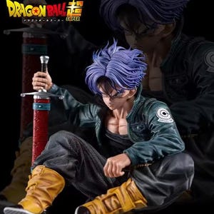 May include: A Dragon Ball Super figure of Trunks with purple hair, wearing a dark green jacket with a Capsule Corp logo, a black shirt, dark pants, and yellow boots. The figure holds a sword with a red scabbard and has a black background.