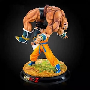 May include: A detailed figurine of two characters from Dragon Ball Z. One character is in an orange and blue outfit, holding another muscular character. The base is black with the Dragon Ball Z logo.