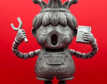 Puede incluir: Una estatua gris estilizada de un bufón con una corona, sosteniendo una honda en una mano y un libro en la otra. La estatua está de pie sobre una base gris de tres niveles.