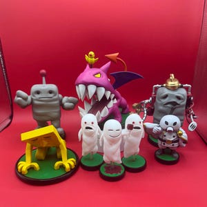 May include: A collection of colorful figurines, including a gray robot, a purple dragon with a yellow bird, and several white ghost-like figures. The figurines are set against a red background, showcasing their vibrant colors and unique designs.