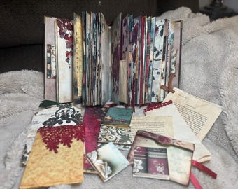 May include: Open journal with aged paper pages and decorative floral prints. Includes various tags, envelopes, and ephemera with lace and ribbon accents. The journal is open, revealing the interior pages.