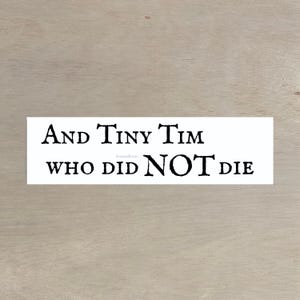 Puede incluir: Una pegatina rectangular blanca con texto negro: "And Tiny Tim WHO DID NOT DIE". El fondo es de veta de madera clara.