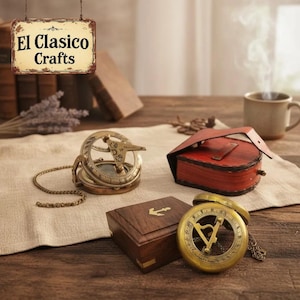 May include: Two brass sundials with chains, one resting on a wooden box with an anchor inlay and the other beside a red leather case. A hanging sign above reads El Clasico Crafts. The items are arranged on a light fabric cloth on a wooden surface.