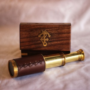 May include: A brass telescope with a brown leather covering and a wooden box with an anchor design. The box is made of dark wood with a natural wood grain.