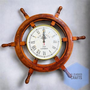 Puede incluir: Reloj de timón de barco de madera con esfera blanca y números romanos. La esfera tiene las palabras "Victoria London 1747". El timón es de madera marrón oscuro.