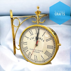 May include: Gold-toned double-sided clock with Roman numerals and the text "Victoria Station Railway Clock London". The clock is mounted on a decorative metal bracket.