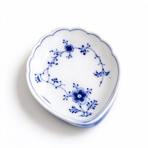 May include: A white porcelain dish with a scalloped edge and a blue floral pattern. The design features delicate hand-painted blue flowers and vines arranged in a circular motif on the interior surface of the small, shallow bowl.