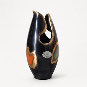 Pode incluir: Um vaso de cerâmica alto de cor castanho-escuro com um acabamento liso e brilhante. O vaso apresenta uma forma orgânica assimétrica com um grande recorte perto do topo. Está decorado com manchas abstratas cor de laranja e verde suave e um autocolante oval prateado com a inscrição Keramik.