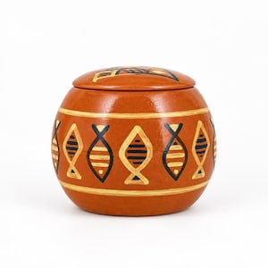 Può includere: Un barattolo in ceramica rotondo color terracotta con coperchio abbinato. L'esterno presenta una fascia orizzontale decorata con un motivo ripetitivo di pesci stilizzati dipinti in nero e crema, delimitata da sottili linee color crema.