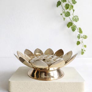 Może przedstawiać: Biały ceramiczny kubek z czarnym uchwytem i napisem "But First, Coffee" pogrubioną, czarną czcionką. Kubek jest umieszczony na rozmytym tle, podkreślając jego czysty design.