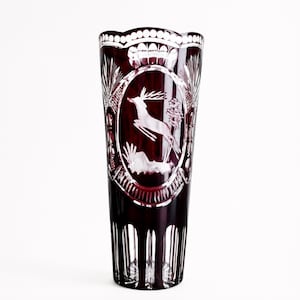 Può includere: Un alto vaso cilindrico in vetro rosso intenso con intricati dettagli in vetro trasparente tagliato. Il centro presenta un medaglione ovale con un motivo inciso di un cervo che salta. Il bordo e la base sono decorati con pannelli verticali.