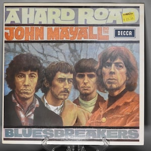 May include: A vintage vinyl record album cover featuring a band called "John Mayall & The Bluesbreakers". The album title is "A Hard Road" and the record label is "Decca". The cover art features a photo of four men in a band, with a forest background.
