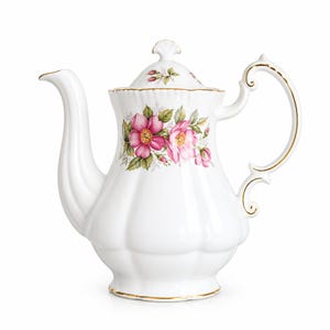 Peut inclure: Une théière en porcelaine blanche avec un corps cannelé et un bord doré. La théière est ornée d'un motif floral de roses sauvages roses et de feuilles vertes sur le devant et sur le couvercle, qui possède un bouton en forme de coquille.