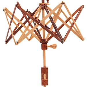 Puede incluir: Un enhebrador de lana de madera con una manivela y una abrazadera para sujetarlo a una mesa. El enhebrador está hecho de madera clara y oscura y tiene un diseño de estrella.