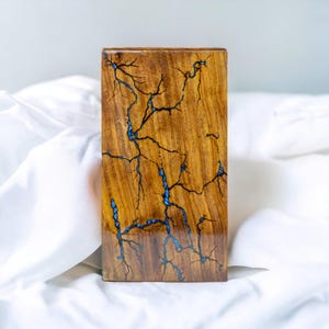 Puede incluir: Un bloque de madera con un diseño de resina azul que se asemeja a rayos. La madera es de color marrón oscuro y la resina es de un azul brillante.