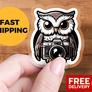 May include: A sticker featuring an owl with a camera. The owl is in grey, white, and black, with large eyes. The sticker has a brown border and the text "FAST SHIPPING".