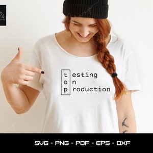 Könnte beinhalten: Weißes T-Shirt mit dem Text "testing on production" in einem schwarzen Kasten.