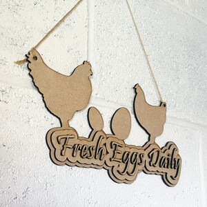 May include: Wooden sign with two chicken silhouettes and the text "Fresh Eggs Daily" hanging from a string. The sign is brown and has a rustic look.