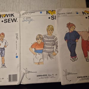 May include: Three vintage Kwik Sew sewing patterns. The patterns feature illustrations of children's clothing designs. The patterns include the text "Kwik Sew" and pattern numbers 2147, 1047, and 1507.