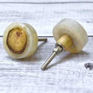 May include: Two round wooden knobs with a light brown wood slice embedded in the centre. The knobs are made of white resin and have a silver metal screw.