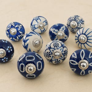 May include: A collection of eleven ceramic cabinet knobs. The knobs are round with a dark blue base and white floral or geometric patterns. Each knob has a silver-colored metal base.