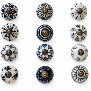 May include: A collection of twelve ceramic cabinet knobs with various blue and white floral and geometric patterns. Each knob has a brass-colored metal base. The knobs are arranged on a white background.