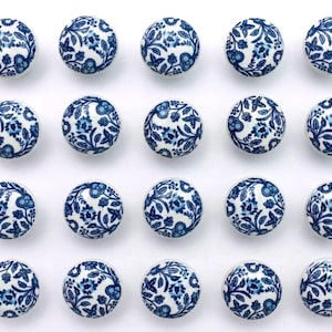 Op de afbeelding: Eenentwintig ronde keramische kastknoppen met een witte basis en een blauw bloemmotief. De knoppen zijn gerangschikt in een rasterpatroon tegen een witte achtergrond. Het bloemmotief bevat bladeren en bloemen.