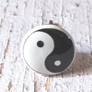Puede incluir: Pomo de cerámica blanco con un símbolo yin yang en blanco y negro.