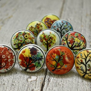 May include: A set of ten ceramic knobs featuring colourful tree designs. The knobs are round and have a white background with various colours, including red, yellow, green, and blue. Each knob features a different tree design with a unique colour scheme.