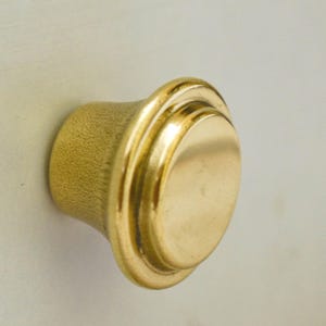 以下が含まれることがあります： 丸みを帯びたわずかに盛り上がったトップとテクスチャ加工されたベースを持つ、金色のキャビネットノブです。