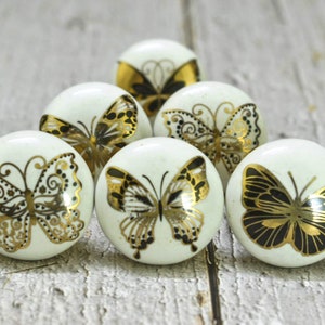 May include: Six white ceramic drawer knobs with gold and black butterfly designs.