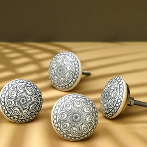 Puede incluir: Cuatro pomos de cerámica con un patrón geométrico en blanco y negro. Los pomos son redondos y tienen un tornillo de metal.