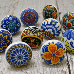 Könnte beinhalten: Zehn Keramikknöpfe mit bunten, komplizierten Mustern in Blautönen, Rot, Gelb und Grün. Die Knöpfe sind rund und haben einen weißen Hintergrund.