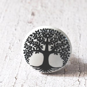 Puede incluir: Pomo de cerámica blanco con un diseño de árbol de la vida negro. El árbol tiene un tronco grueso y muchas ramas con hojas.