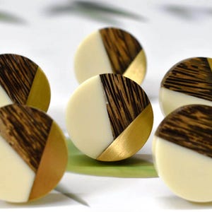 Peut inclure: Six boutons décoratifs ronds en bois et or avec un fond blanc. Les boutons sont en bois avec un grain brun foncé et des accents dorés.