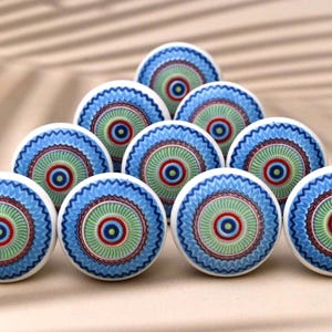 Op de afbeelding: Een set van tien keramische knoppen met een blauw, groen en rood mandala-ontwerp. De knoppen zijn rond en hebben een witte achtergrond.