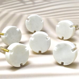 May include: Six white marble cabinet knobs with a brass screw. Each knob has a circular shape with a geometric design.