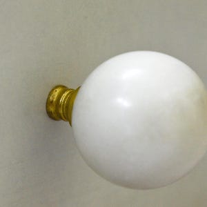 Pode incluir: Um botão de armário de mármore branco com base de metal dourado.